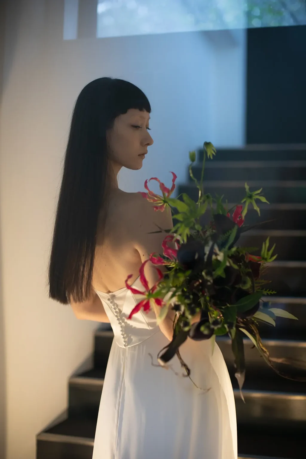 スレンダーラインのウェディングドレスを着て赤い花のブーケを持つ女性の後ろ姿