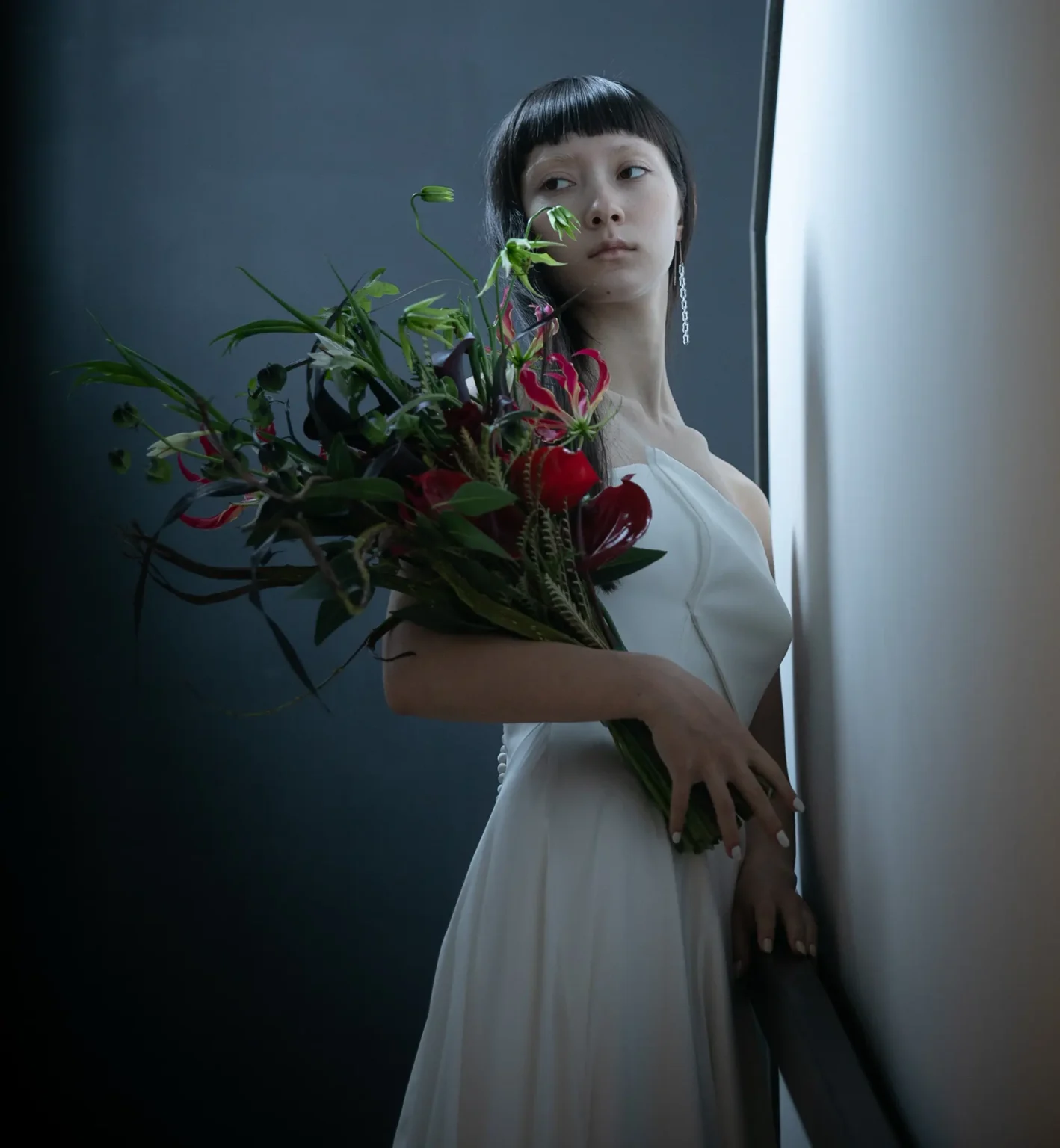 スレンダーラインのウェディングドレスを着て赤い花のブーケを持つ女性