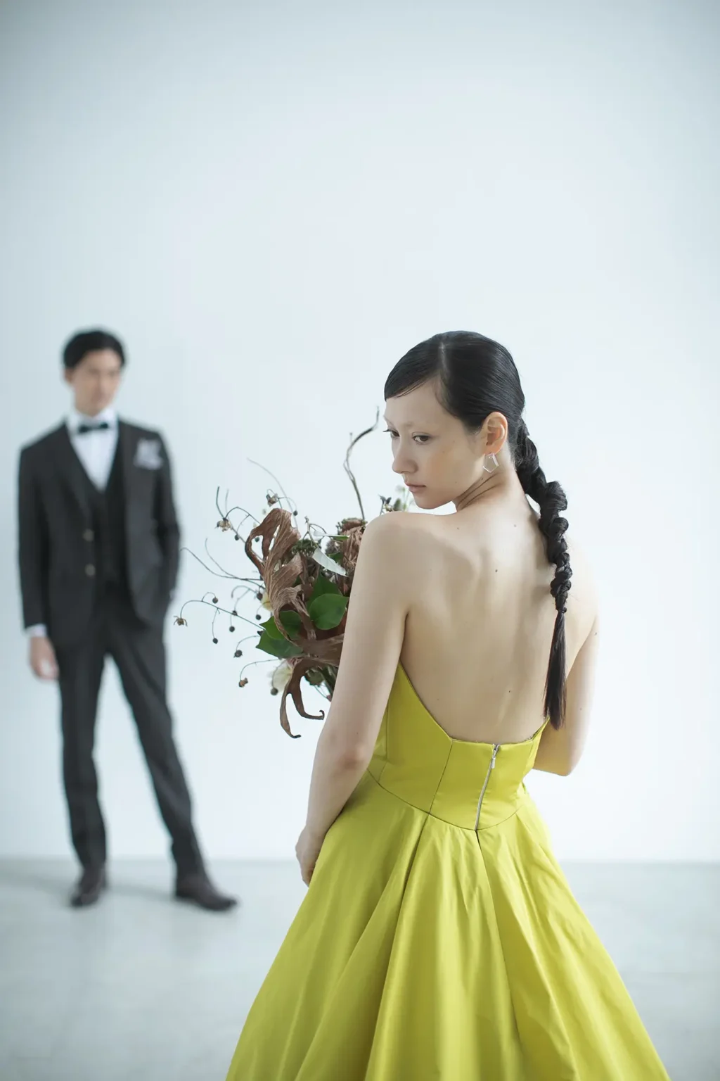 鮮やかなイエローのカラードレスを着てブーケを持つ新婦とタキシードを着た新郎