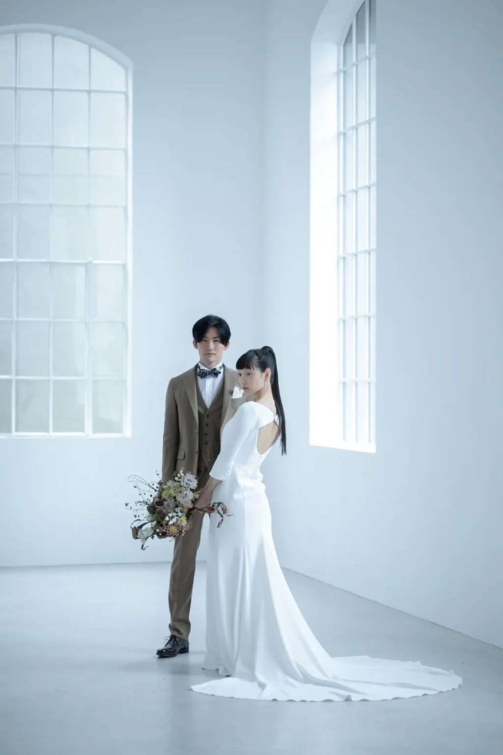 長袖のマーメイドシルエットのウェディングドレスを着た女性とブラウンのスリーピースを着た男性