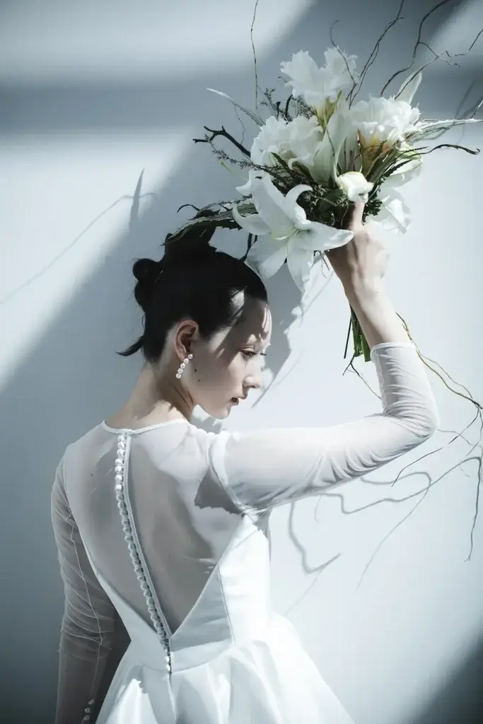 白い花のブーケを持つ長袖シースルーのウェディングドレス姿の女性