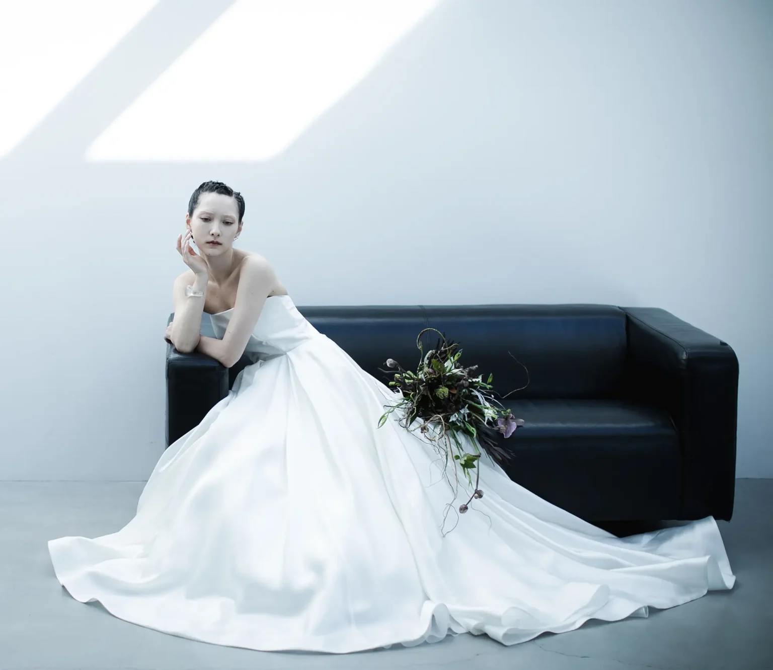 大ぶりのブーケと一緒にソファに座ってポーズをとるウェディングドレス姿の女性