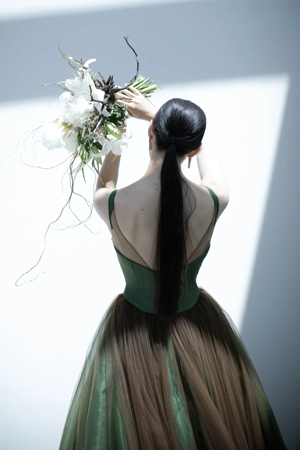 動くたびに色の濃淡が生まれ、一瞬ずつ新たな表情を見せる、グリーンにブラウンのチュールを重ねたカラードレスの後ろ姿