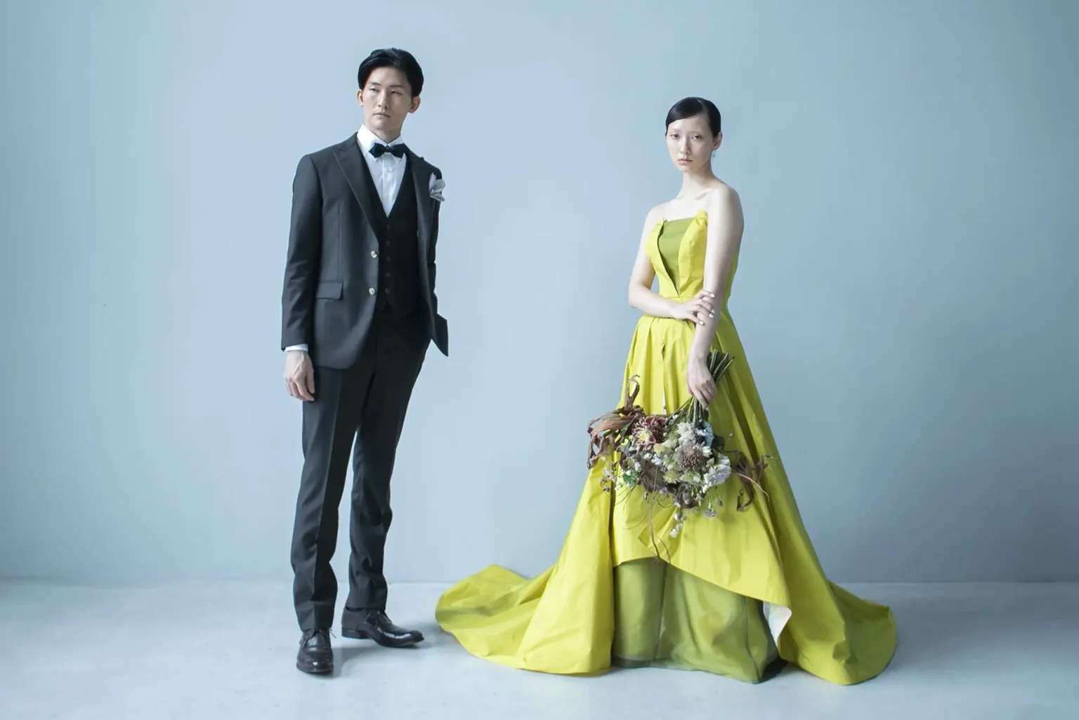 鮮やかなイエローのカラードレスを着てブーケを持つ新婦とタキシードを着た新郎