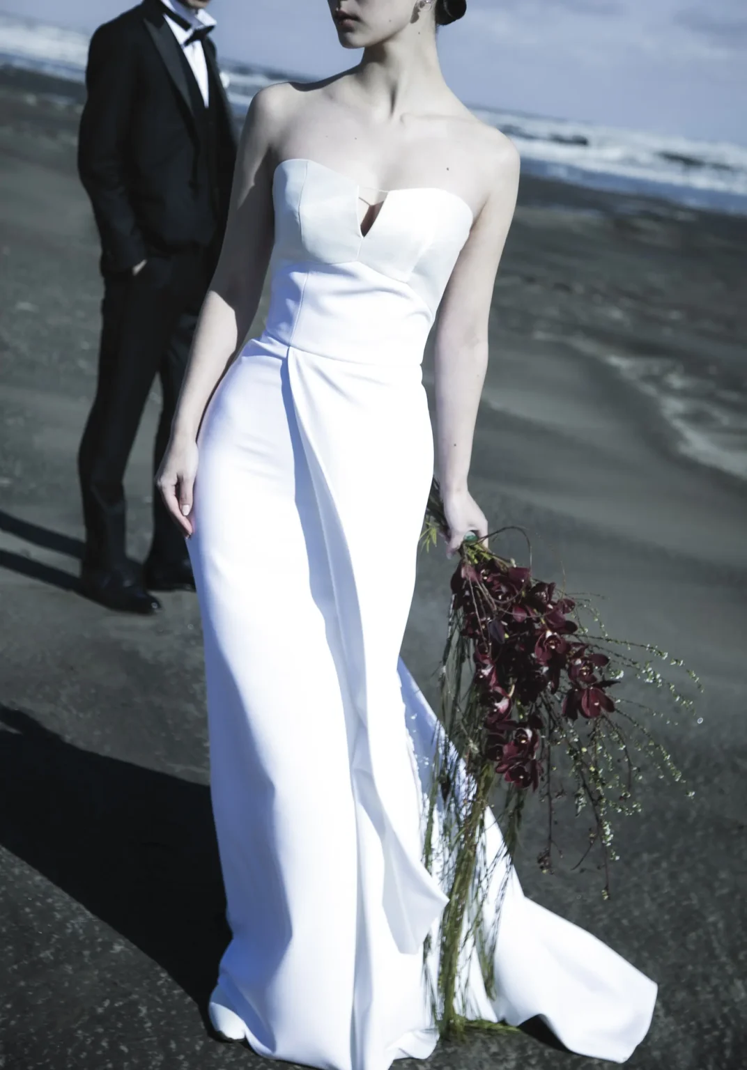 マーメイドラインのシンプルなウェディングドレスを着て浜辺を歩く花嫁